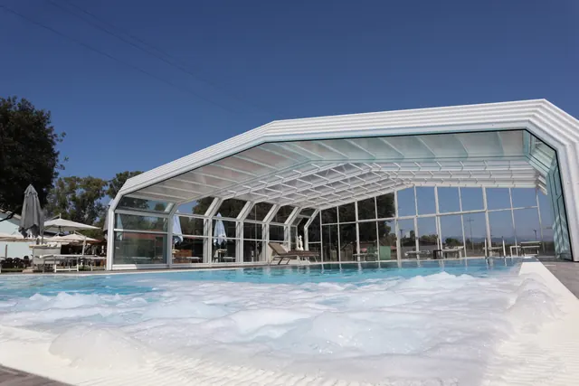 La piscina con la copertura mobile di vetro aperta, l'idromassaggio acceso e gli ombrelloni sul prato