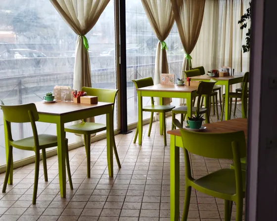 La sala da tè: tavolini di legno con le sedie verde mela, davanti alle vetrate con le tende