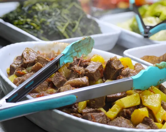 Il banco della tavola calda: spezzatino con patate, verdure e le pinze per servirsi