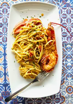 Linguine all’astice su un piatto bianco, sulla tovaglia a maioliche
