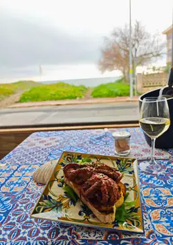 Polpo alla griglia su una bruschetta e un calice di bianco, con il lungomare oltre la vetrata