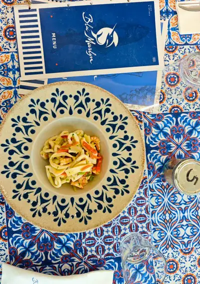 Un piatto di pasta ai frutti di mare sulla tovaglia a maioliche, accanto al menù blu del Blu Marlyn