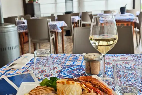 La veranda del ristorante: i tavoli con le tovaglie a maioliche, un calice di bianco e una grigliata di pesce
