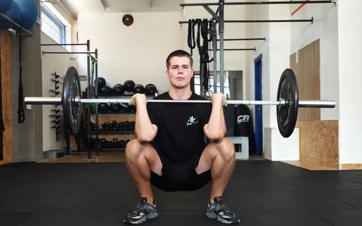 Un ragazzo con la maglia Body Planet fa uno squat con il bilanciere