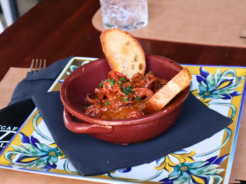 Moscardini al sugo in un coccio di terracotta, con due crostini, su un vassoio di maiolica