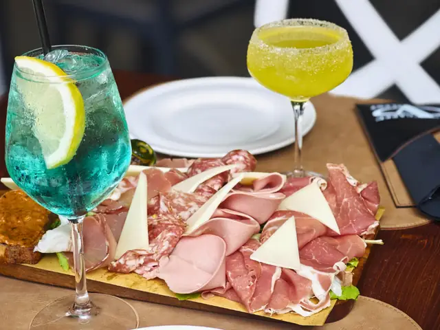 Uno spritz azzurro e un cocktail giallo accanto a un tagliere di salumi e formaggio