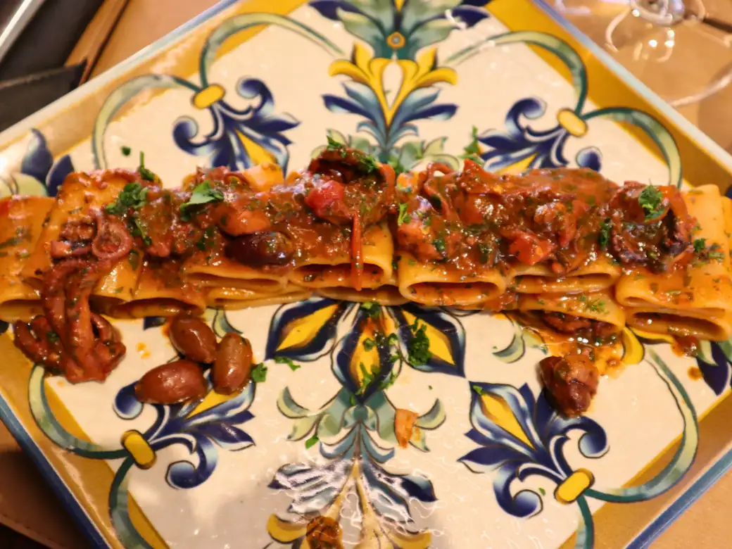 Paccheri al sugo di polpo con olive, su un piatto di maiolica gialla e blu