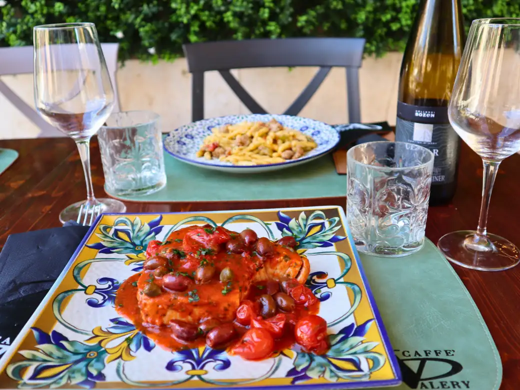 Un trancio di pesce con pomodorini, olive e capperi, servito sul tavolo all’aperto