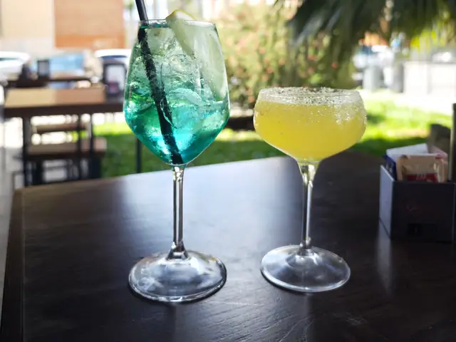 Uno spritz azzurro e un cocktail giallo sul tavolo all’aperto, fra le palme