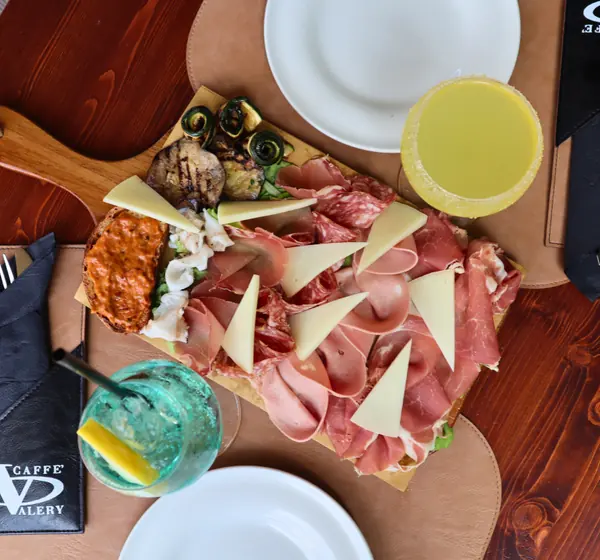 Il tagliere dell’aperitivo visto dall’alto: salumi, formaggio, verdure grigliate, un crostino e i drink