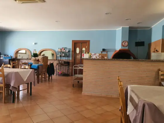 La sala interna, con le pareti azzurre, i tavoli apparecchiati e il forno a legna dietro il bancone