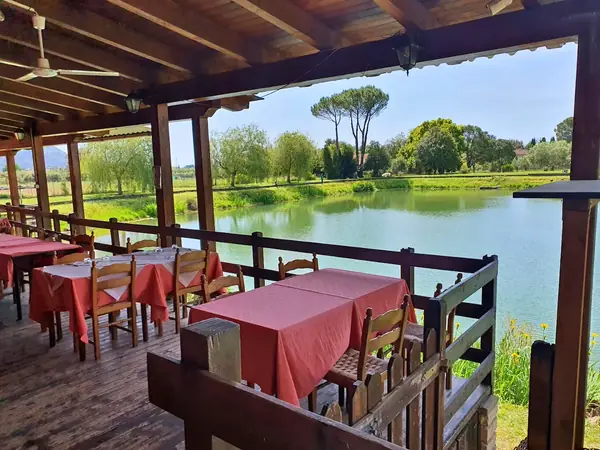 La terrazza coperta del ristorante, con i tavoli apparecchiati affacciati sul laghetto fra gli alberi