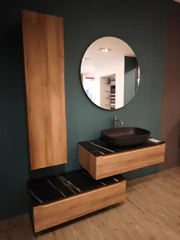 Mobile bagno in legno con lavabo nero e specchio tondo, su una parete verde