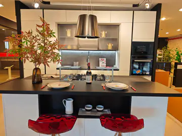 Cucina bianca con isola scura, cappa a campana e sgabelli rossi