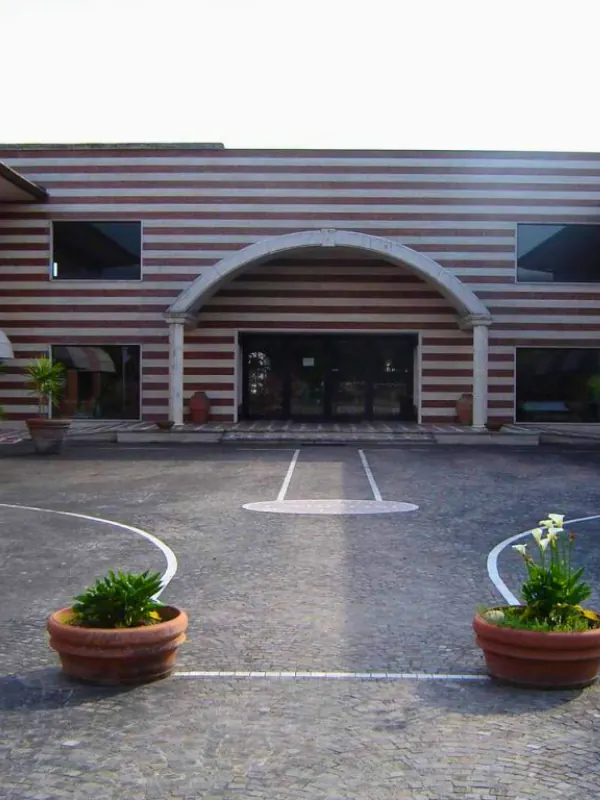 L'ingresso dello showroom: la facciata a fasce rosse e chiare con un grande arco, e due vasi di fiori sul piazzale