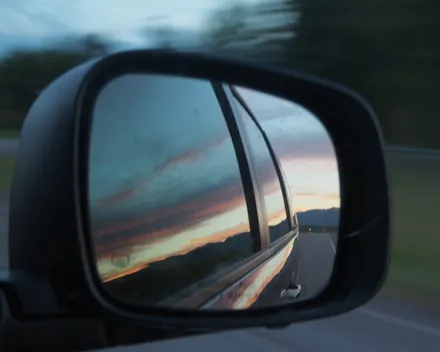 Lo specchietto laterale di un'auto in corsa, con il cielo del tramonto riflesso