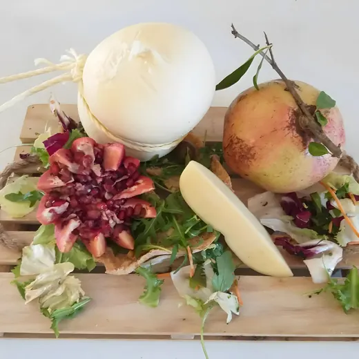Una mozzarella di bufala su una cassetta di legno, con melagrane, una fetta di formaggio e insalata