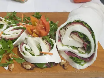 Rotoli di mozzarella farciti con salumi e verdure, su un tagliere