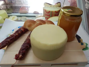 Una forma di formaggio con salsicce stagionate, pane intrecciato e un vasetto di miele