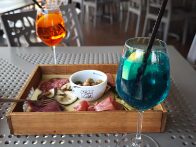 Tagliere di salumi e olive con uno spritz e un cocktail blu