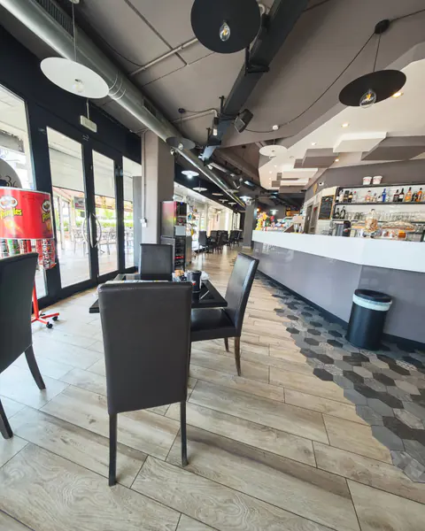 Il lungo bancone bianco del bar, con i tavolini neri e il pavimento a esagoni