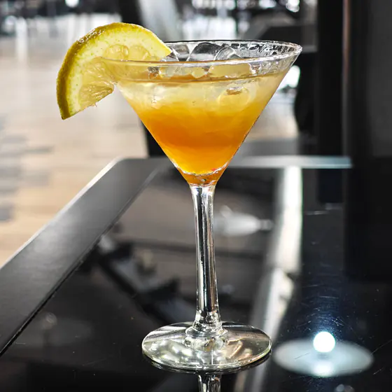 Un cocktail ambrato in coppa Martini, con una fetta di limone, sul bancone scuro
