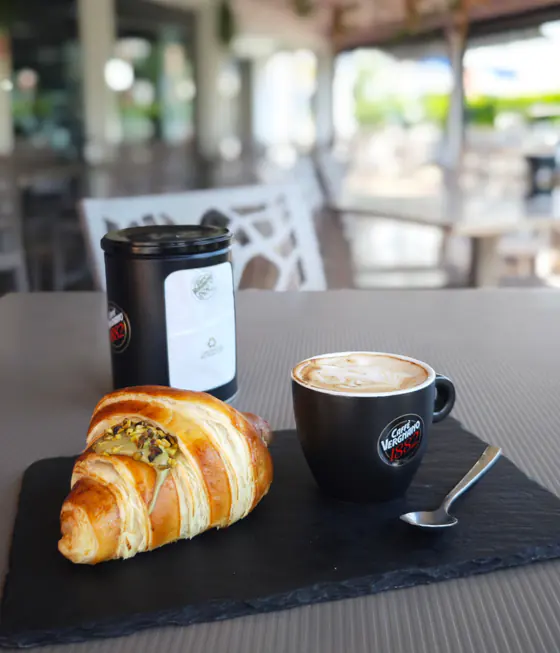 Cornetto al pistacchio e cappuccino sul tavolo della terrazza, accanto a una latta di caffè