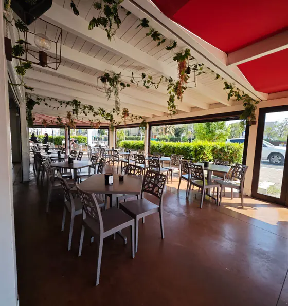 La terrazza coperta di Civico 36, con le tende rosse, le piante appese e i tavoli apparecchiati