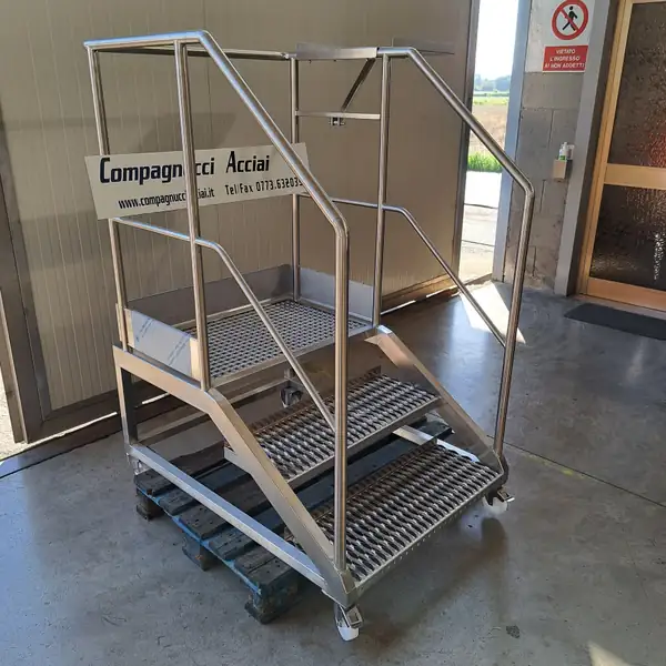 Scala mobile in acciaio inox con gradini grigliati e corrimano, con il marchio Compagnucci Acciai