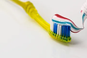 Uno spazzolino giallo su cui scende il dentifricio a righe
