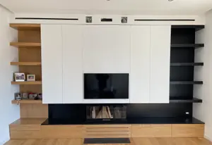 Parete attrezzata con ante bianche, mensole in legno e nere e il camino sotto la televisione