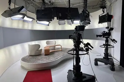 Due telecamere da studio puntate su un salotto televisivo, sotto i proiettori