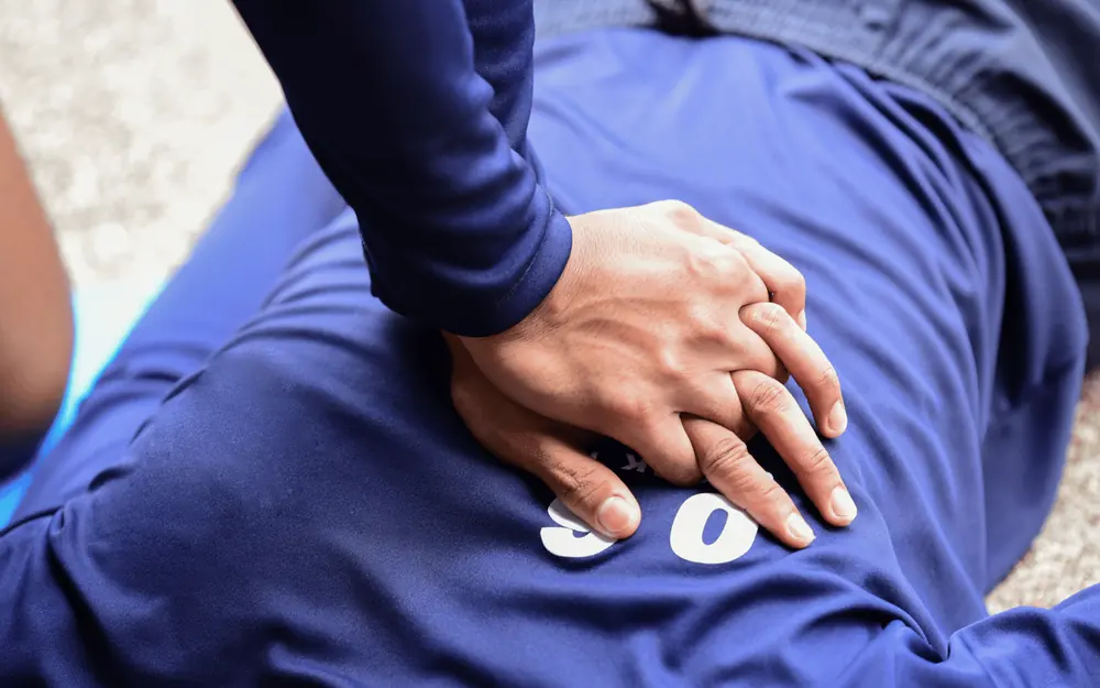 Le mani di un soccorritore, una sull'altra, sul petto di una persona distesa: il massaggio cardiaco