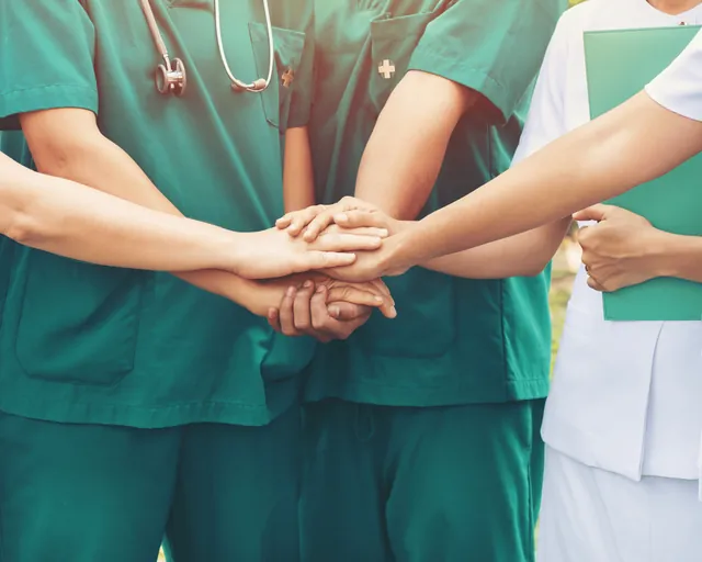 Operatori sanitari in divisa verde e bianca con le mani unite al centro