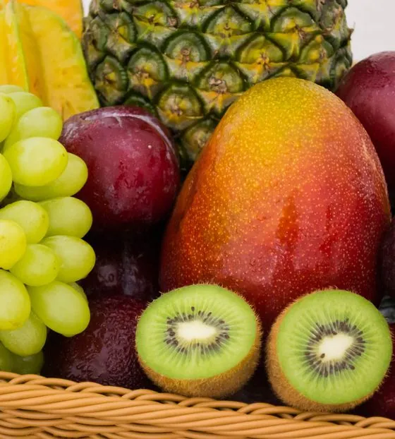 Un cesto di frutta fresca: uva bianca, mango, kiwi tagliati, prugne, mele e ananas