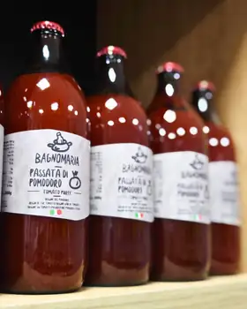 Bottiglie di passata di pomodoro in fila su uno scaffale di legno