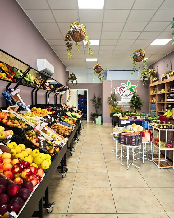 L'interno del negozio: a sinistra i banchi di frutta e verdura, a destra gli scaffali di legno con conserve e vini, cestini di fiori appesi al soffitto