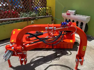 Una trinciatrice arancione con il braccio idraulico, pronta nel cortile