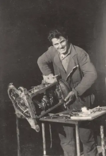 Foto d'epoca: un meccanico sorridente al lavoro su un motore smontato