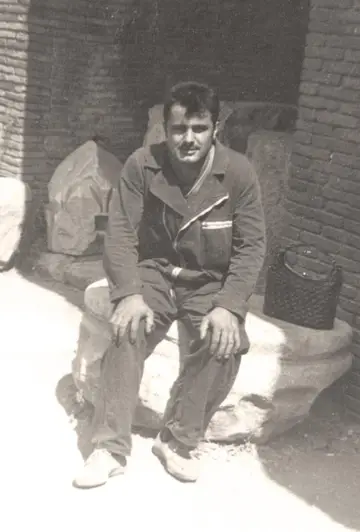 Foto d'epoca: un giovane in tuta da lavoro, seduto davanti a un muro di mattoni