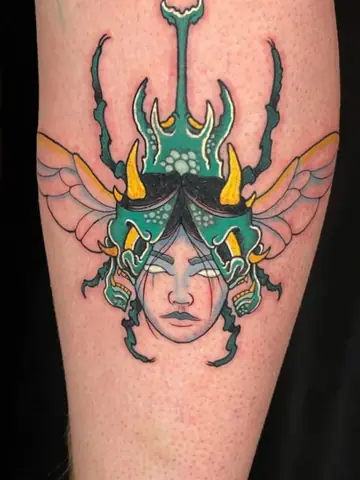 Uno scarabeo verde con un volto di donna, a colori sulla gamba