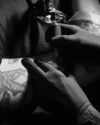 Le mani guantate di un tatuatore al lavoro con la macchinetta