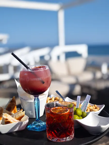 Due cocktail e gli stuzzichini dell’aperitivo, con il mare sullo sfondo