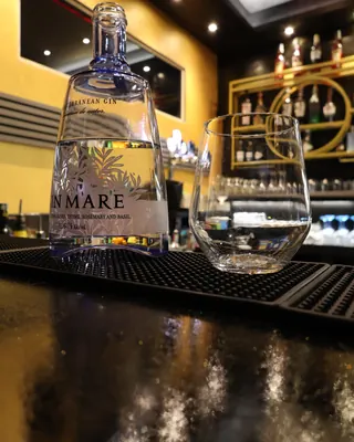 Una bottiglia di gin e un bicchiere sul bancone, davanti agli scaffali dorati del bar