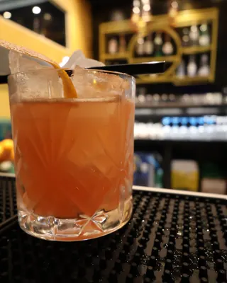Un cocktail ambrato con una scorza d’arancia, sul bancone