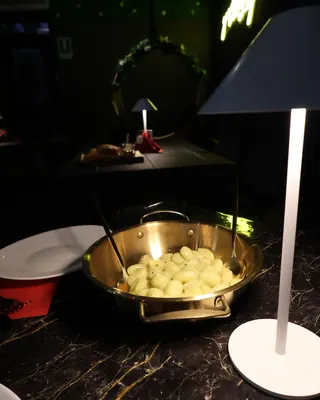 Gnocchi in una padella dorata, su un tavolo di marmo nero accanto a una lampada