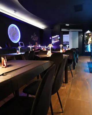 La sala con i tavoli apparecchiati, le lampade accese e la grande luna luminosa sulla parete