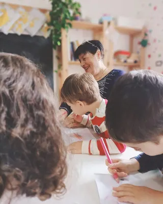 Una nonna disegna insieme ai bambini attorno al tavolo