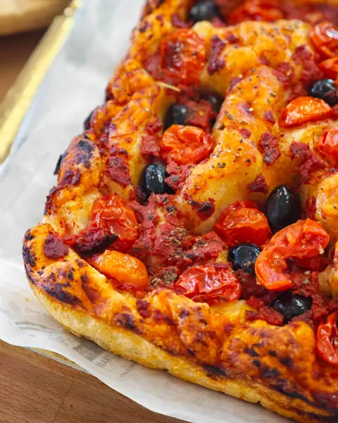 Una teglia di pizza con pomodorini e olive nere