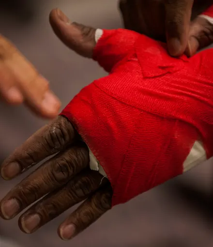 Una mano avvolta in una benda rossa prima del combattimento, su fondo scuro
